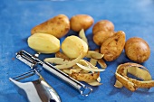 Potatoes and peel potatoes with vegetable peeler on blue background