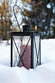 Tin lantern with red candle in snow