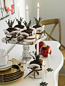Schokomuffins in Papiermanschette auf silbernem Kuchenständer; gestapelte goldene Teller, Kerzen und Weihnachtsdeko