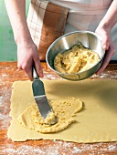 Paste being applied on dough with spatula while preparing almond kringle, step 1