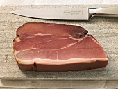 Close-up of slice of ham and knife on cutting board