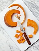 Pieces and slices of squash on cutting board with knife, overhead view
