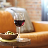 Glass of red wine with green olives in bowl on wooden table