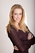 Portrait of pretty blonde woman wearing brown top standing with arms crossed, smiling