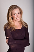 Portrait of pretty blonde woman wearing brown top standing with arms crossed, smiling