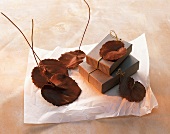 Schokolade, kleine Schachteln, obenauf + daneben Schokoladenblätter