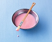 Macarons, rosa eingefärbter Zuckerguß in Schale, Pinsel mit Guß