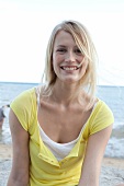 Cheerful blonde woman wearing yellow top at beach, smiling