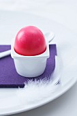 A pink Easter egg in a simple egg cup on a purple place mat