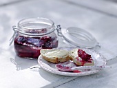 Plum jam in preserving jar and slice of baguette on plate