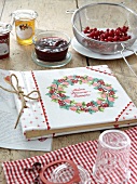 Homemade recipe album, jam and cheery in strainer on table