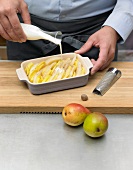 Pouring cream on pears in baking dish for preparation of pear gratin