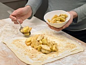Hand putting apple pieces on rolled up dough for preparation of puff pastry, step 1