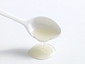 Glucose syrup being poured from spoon on white background