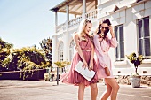 Two cheerful women wearing short pink dresses walking on pavement