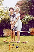 Two women wearing short summer dress playing croquet at garden