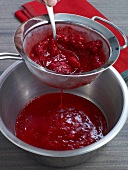 Passing raspberries from sieve with spoon for preparation of sauce, step 1