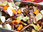Adding vegetables in roasted veal in baking tray for preparation of veal stock, step 4
