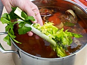 Adding tied herbs in mixture in pan for preparation of veal stock, step 8