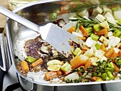 Close-up of vegetables being stirred in pan for preparation of bratenjus, step 1