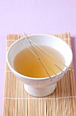 Acupuncture needles on white bowl with liquid kept on wooden mat