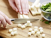 Bread being cut into small cubes on wooden chopping board for salsa verde