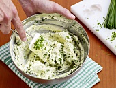 Close-up of hand mixing herbs and butter in bowl, step 2