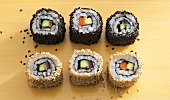 Sushi covered with black and white sesame seeds on yellow background