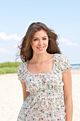 Portrait of pretty brunette woman wearing floral pattern top standing on beach, smiling