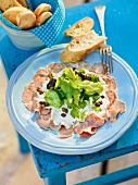 Slices of veal on plate and bread slices in container, garden kitchen