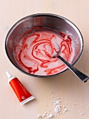 Frosting with red food colour being mixed with spoon