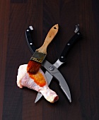 Chicken thigh, poultry gelschere and brush with marinade on wooden surface