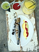 Sardines on wooden board with three sauces, overhead view