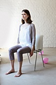 Pretty woman wearing white top, shrug and crop pants sitting upright in chair