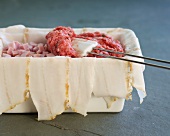 Terrine mould being filled with minced meat using spatula, step 2