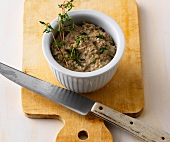 Bowl of spicy liver spread on wooden board with knife