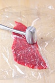 Meat being beaten with meat tenderizer for preparation of sauces and dips, step 1