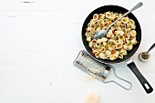 Orecchiette pasta with olive pesto in pan beside grater on white background