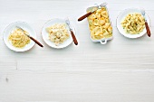 Four plates with different types of cheese pasta on white background