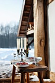 Stew and a candleholder on wooden table in front of a wintry hut