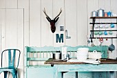 A country house style kitchen with a bench, a table, a wall shelf and antlers on the wall