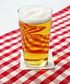 Bier in Glas mit wenig Schaum steht auf Tischdecke.