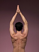 Rear view of man with hands raised in prayer position while performing yoga