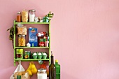 Various food stocked on green shelf against pink wall