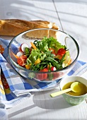 Mixed summer salad in glass bowl with dressing on side