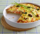 Vegetables and ham quiche in serving dish on wooden tray