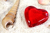 Close-up of sea shell and red heart on sand
