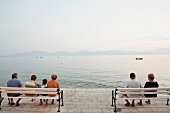 Rear view of people sitting on bench near sea, Makarska, Croatia