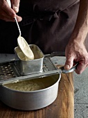 Close-up of dough being put through spaetzle maker while preparing spaetzle, step 2