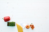 Pepper, herbs, raw pasta, paper and tomatoes on white background